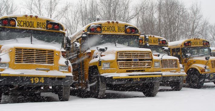 4 parked school buses with snow falling