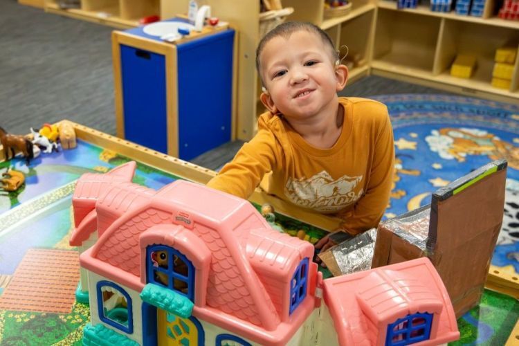 Young boy with hearing aids playing with toys in a classroom.